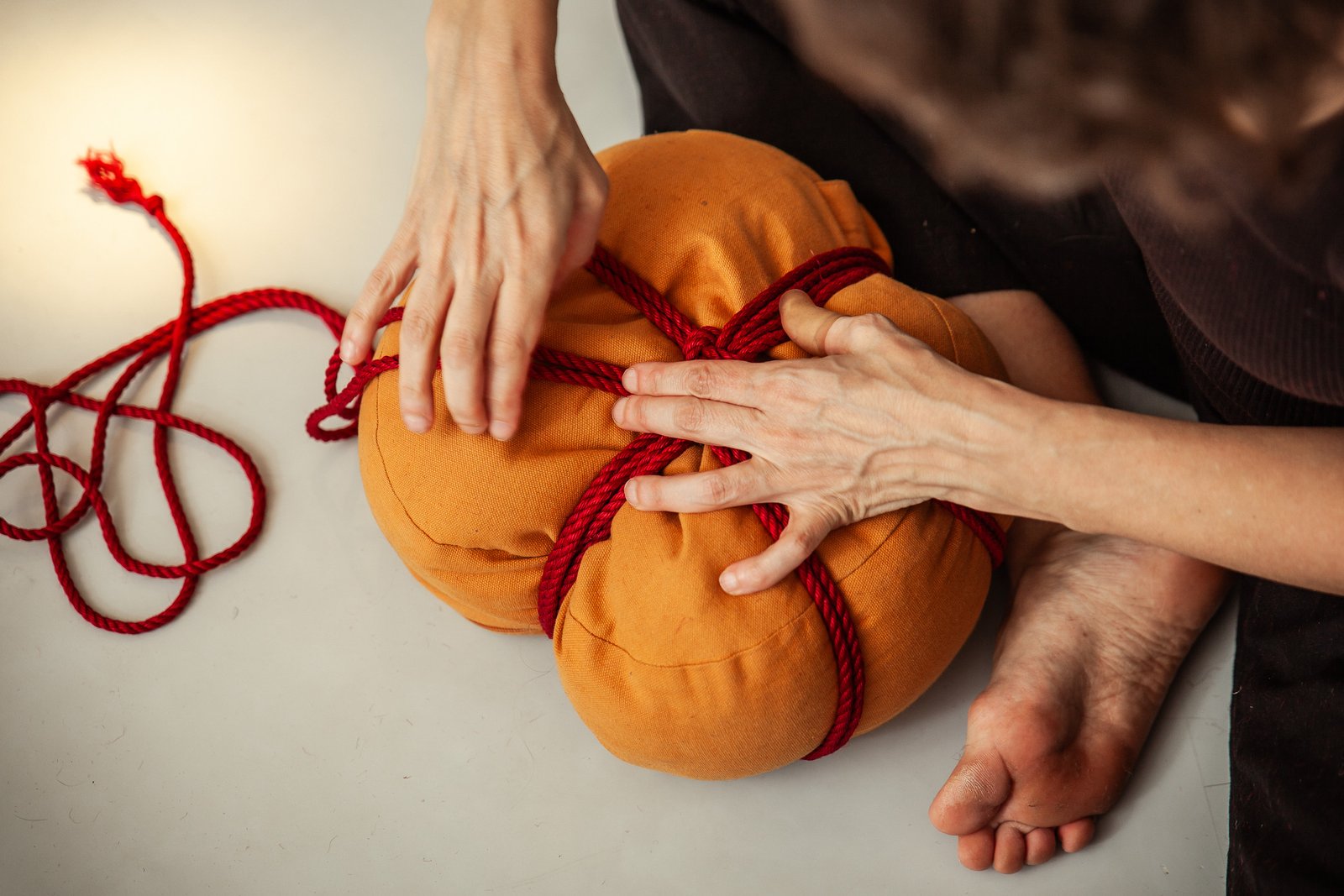 Hands tying red rope around orange cushion
