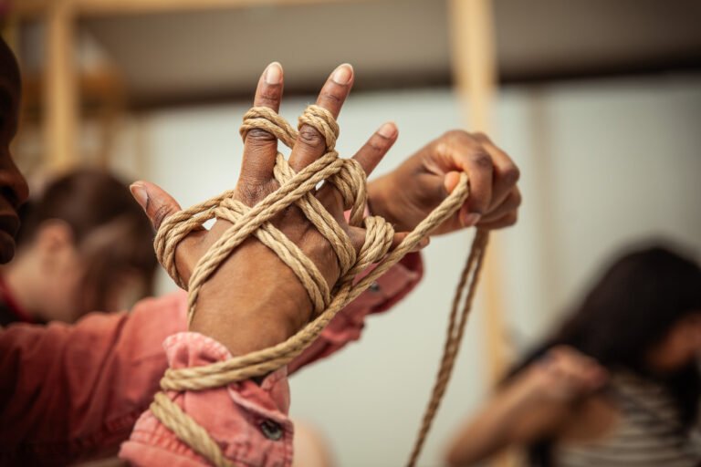 Hands tying intricate rope design.