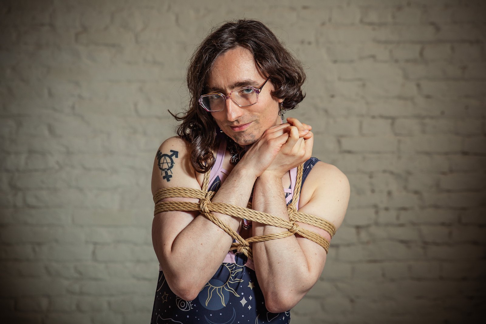 Person with glasses tied with rope, tattoo visible.