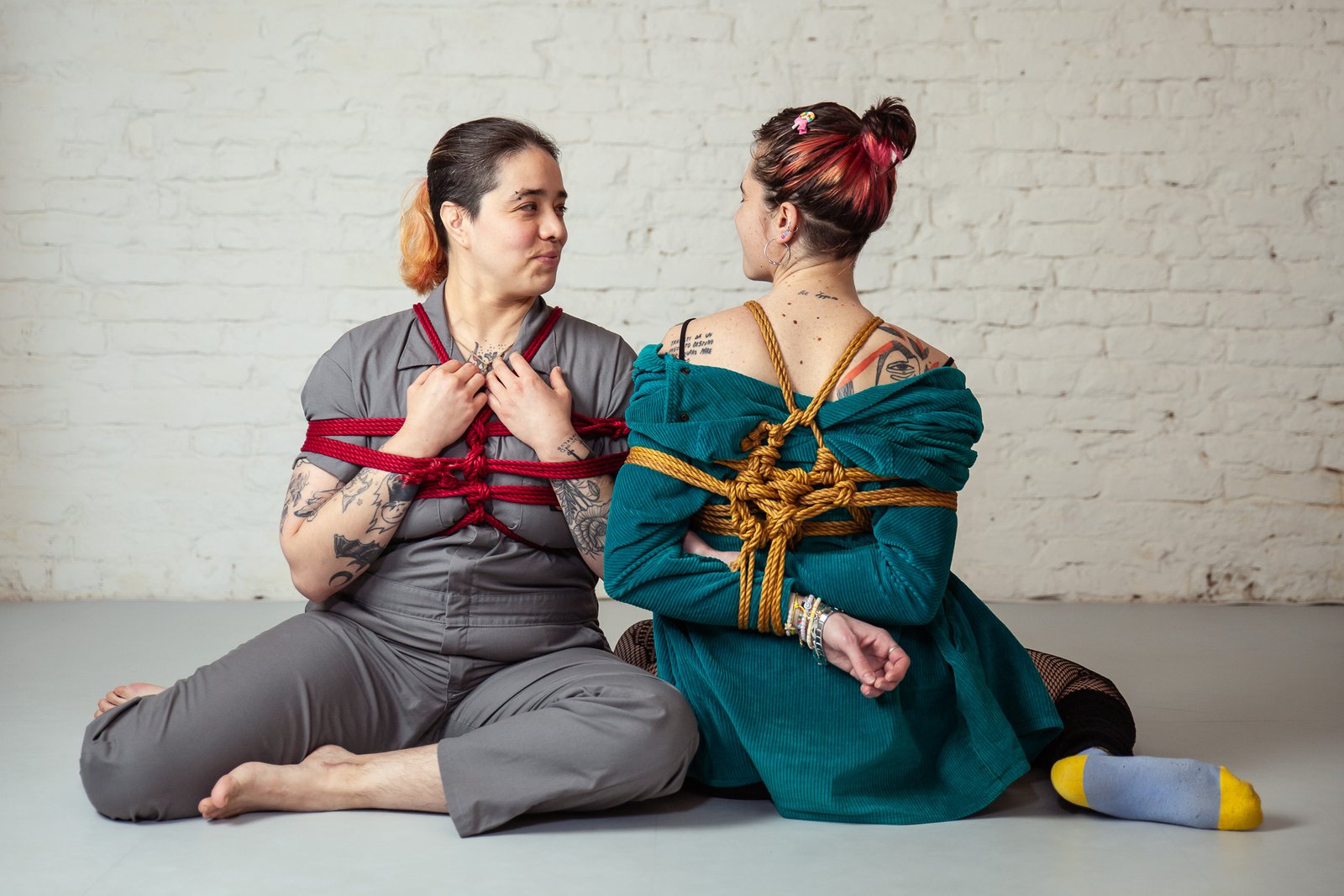 Two people sitting in artistic rope bondage.