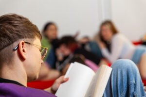 Person reading book with others in background.