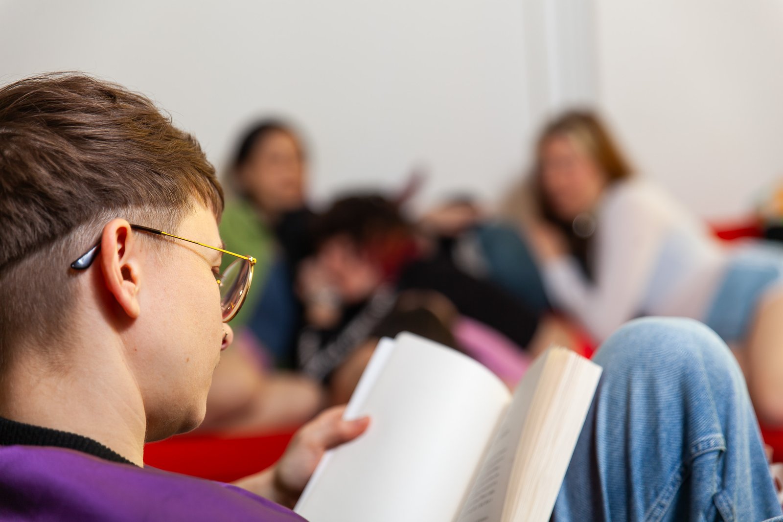 Person reading book with others in background.