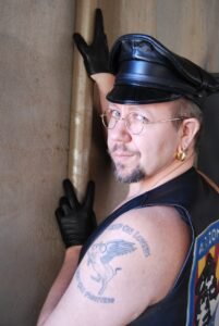 Person in leather hat and vest, tattoo visible.