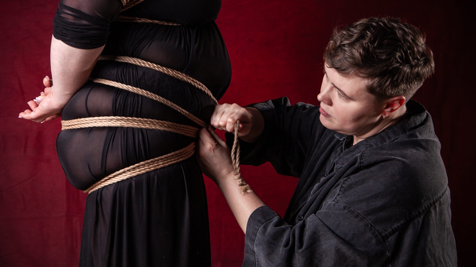 Person tying rope on someone wearing black dress.