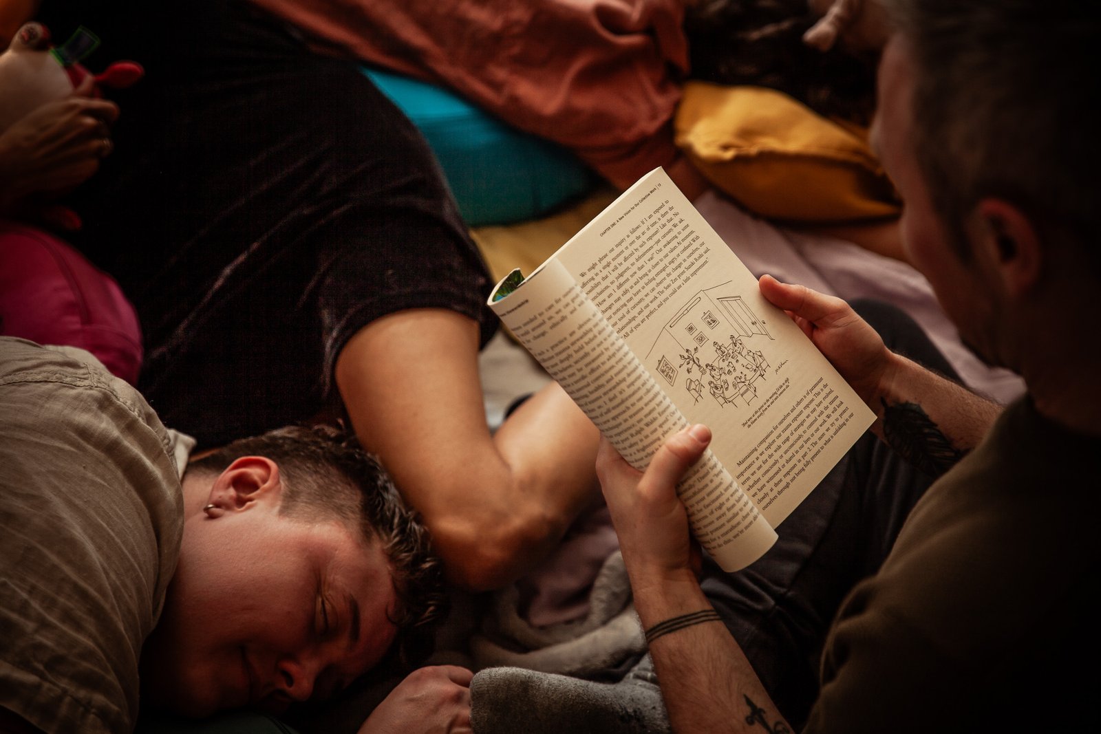 mg 6950 Person reading book while others sleep nearby.