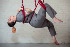 Person suspended in red ropes doing aerial yoga.