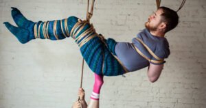 Person wearing mermaid tail suspended by ropes indoors.