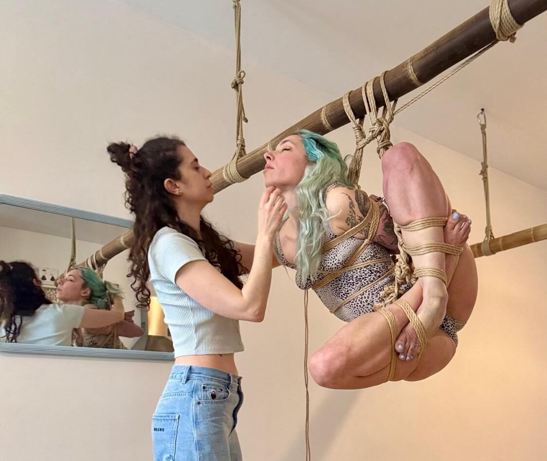 Person suspended in rope, another assists nearby.