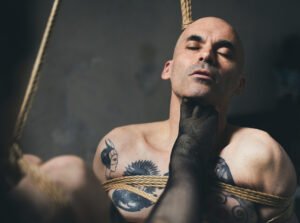 Bound man with tattoos and rope on torso.