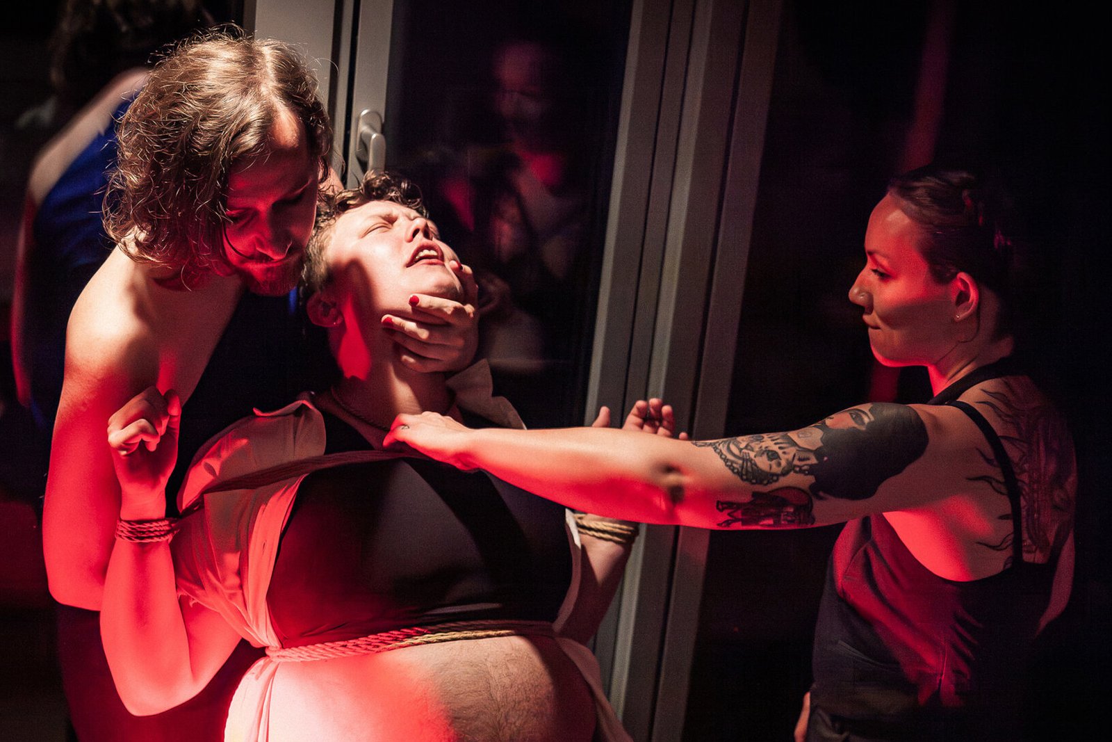 Two people restraining woman under red lighting