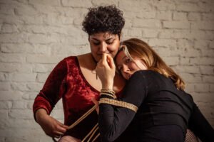 Two women embrace with rope wrapped around torso