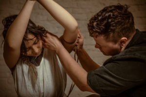 Person tying rope around another's arms indoors.
