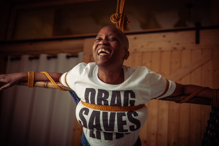 Person smiling while tied with ropes indoors.