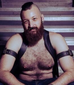 Man with beard and leather gear sitting on stairs.