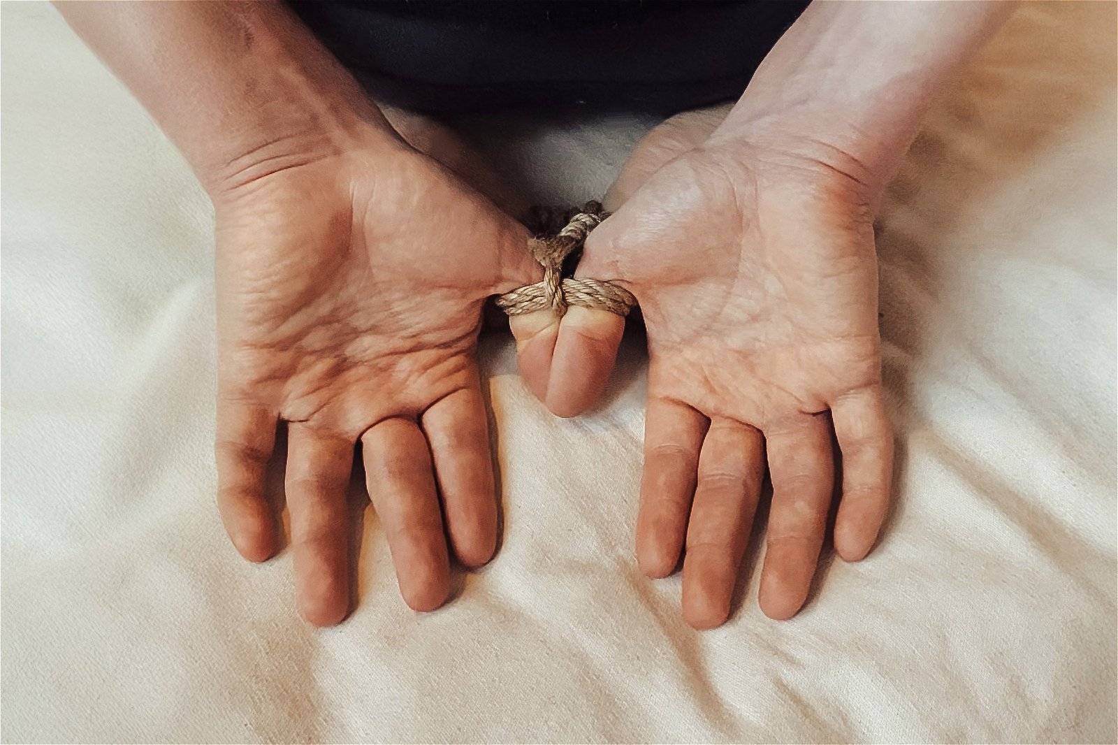 Hands tied with rope on fabric surface
