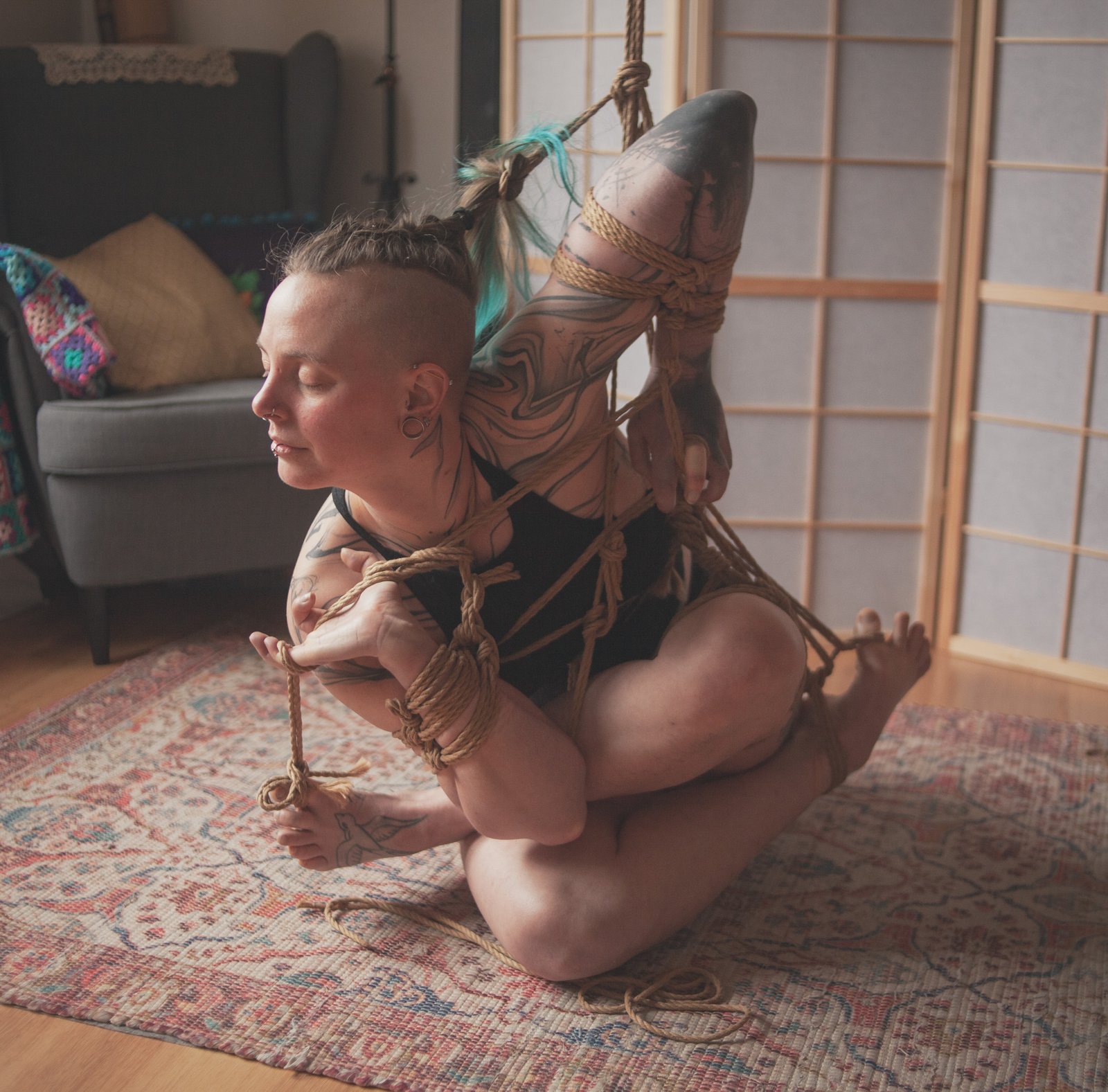 Person in intricate rope bondage pose indoors.