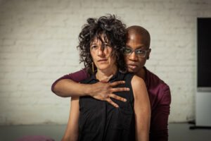 Two people embrace against a white brick wall.
