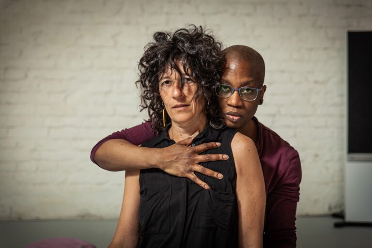 Two people embrace against a white brick wall.