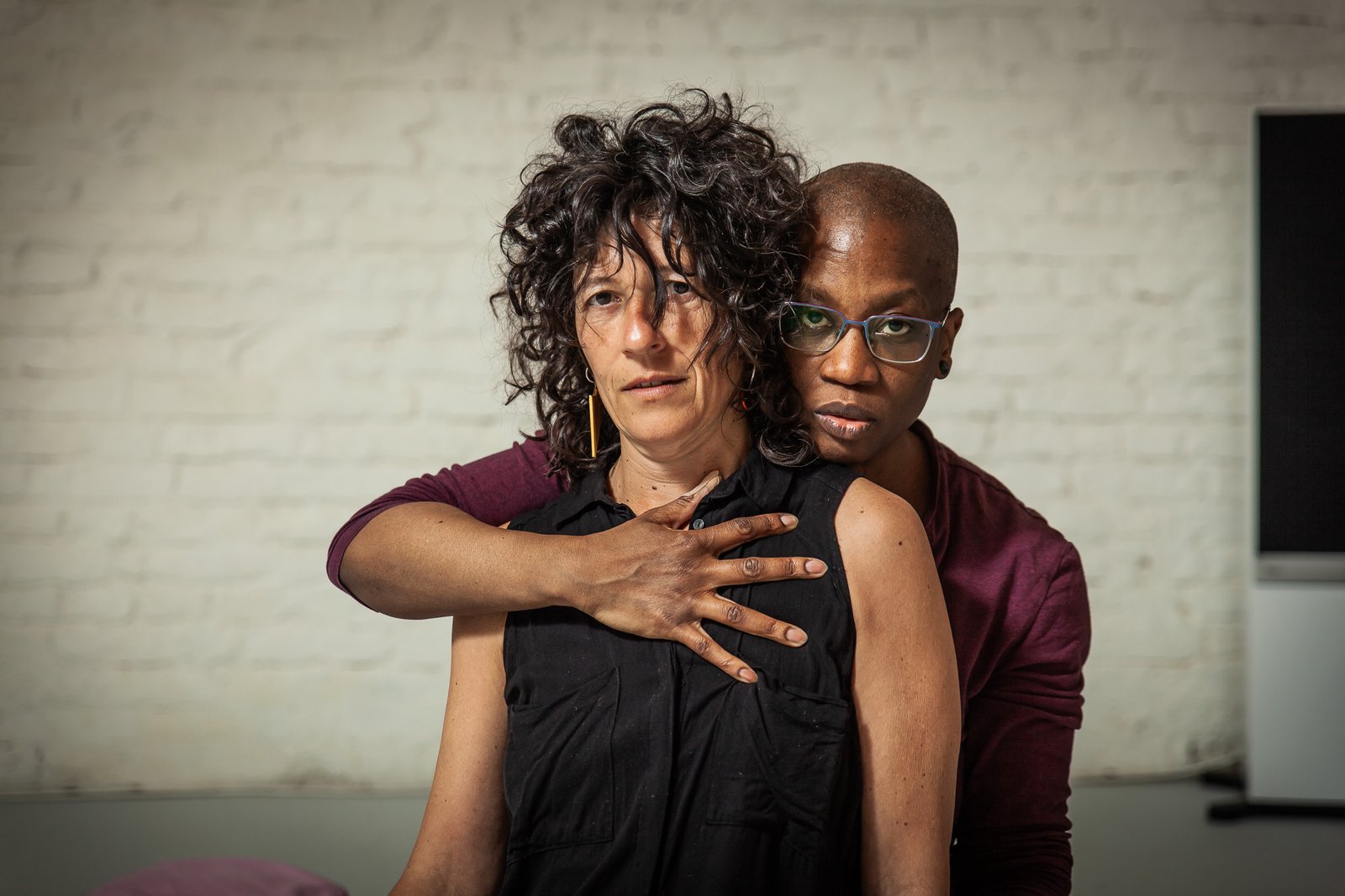 Two people embrace against a white brick wall.
