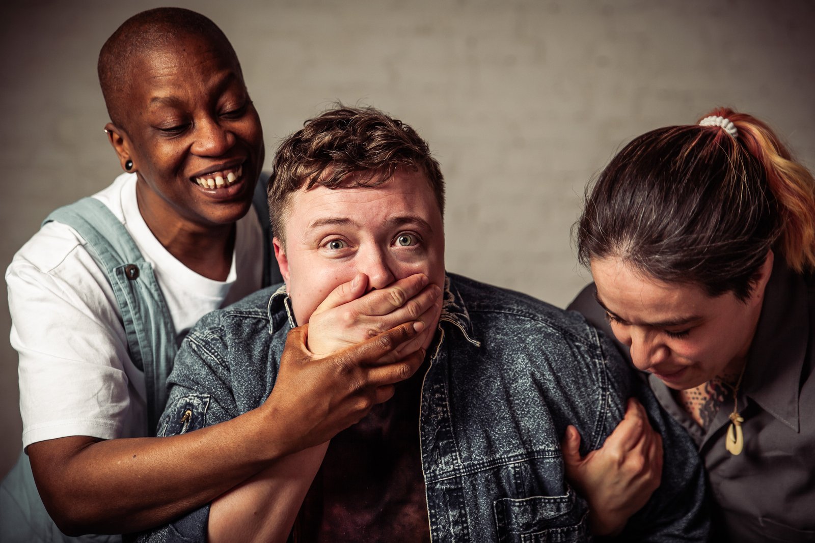 Three people laughing while covering someone's mouth.