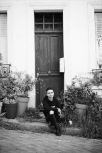 Person sitting on steps by a door with plants.