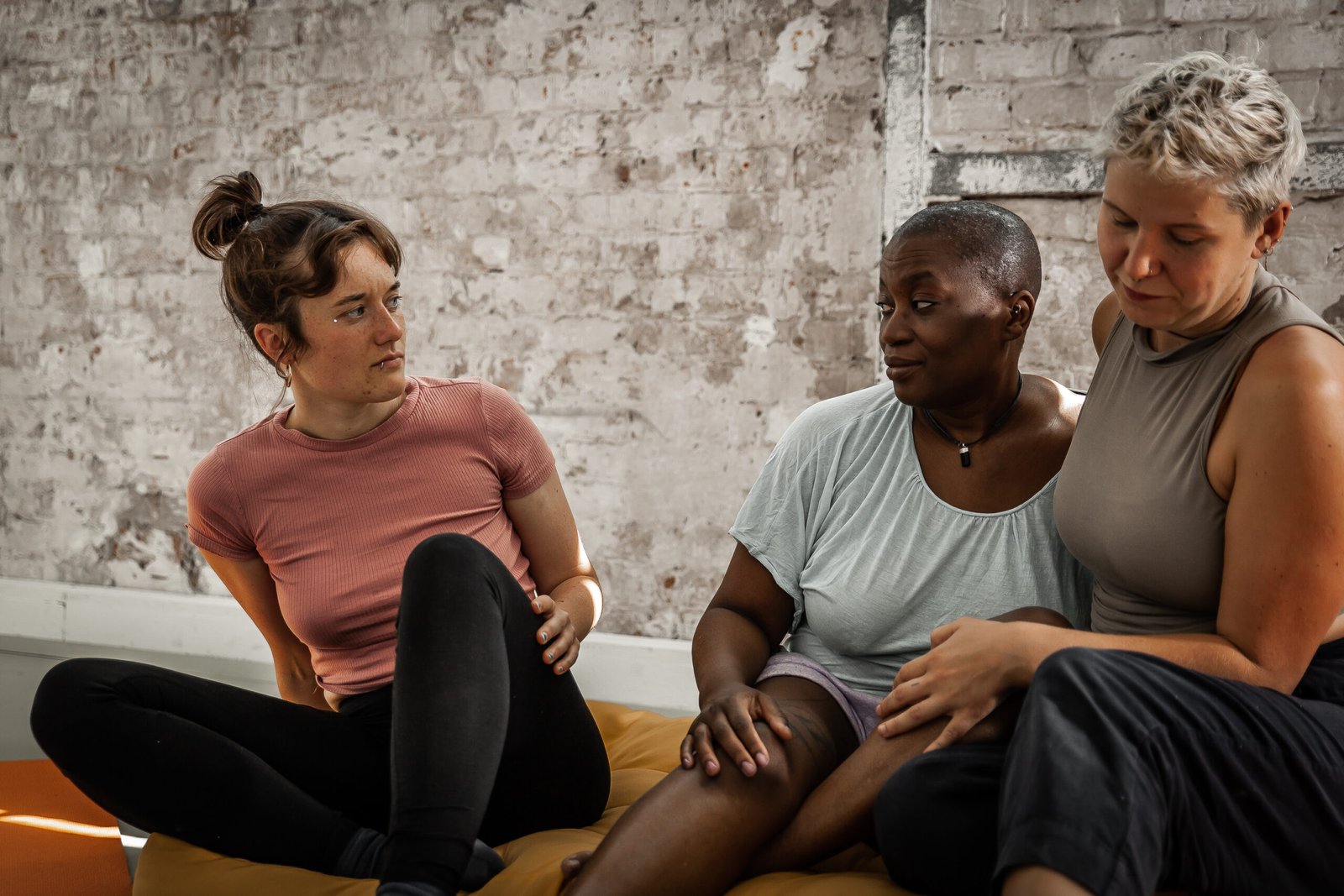 Three people talking on yoga mats indoors.