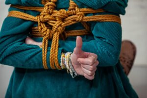 Person in teal rope bondage, thumbs up gesture.