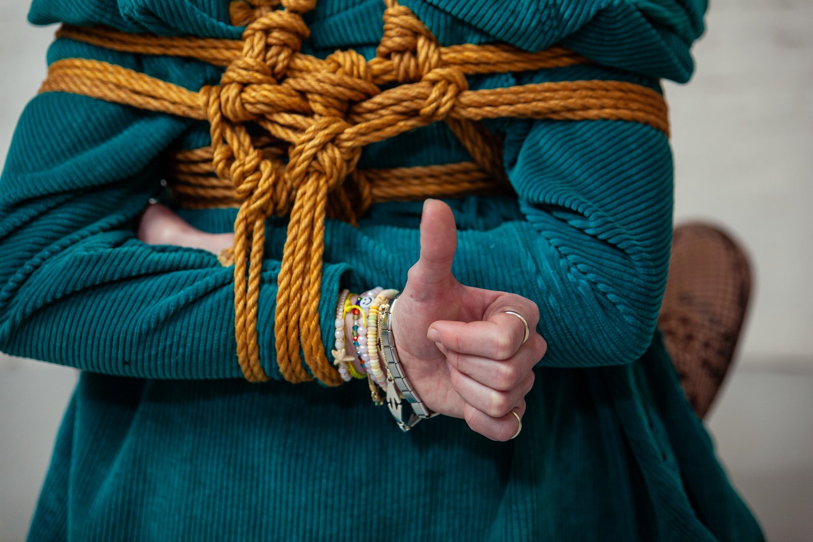 Person in teal rope bondage, thumbs up gesture.