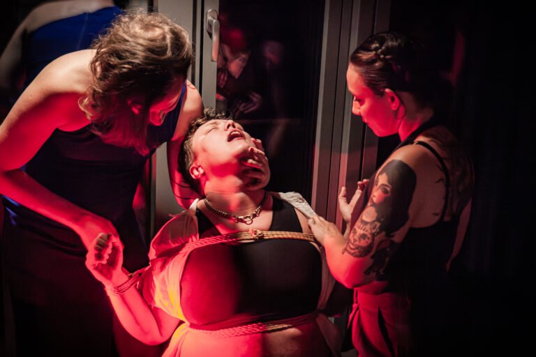 Dramatic bondage scene with three individuals.