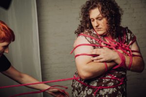 Person bound with red rope indoors