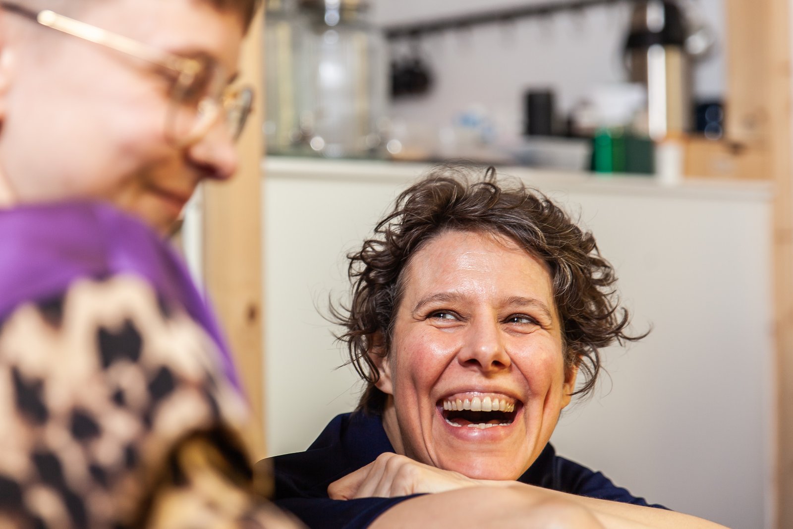 Two women laughing together in a bright kitchen