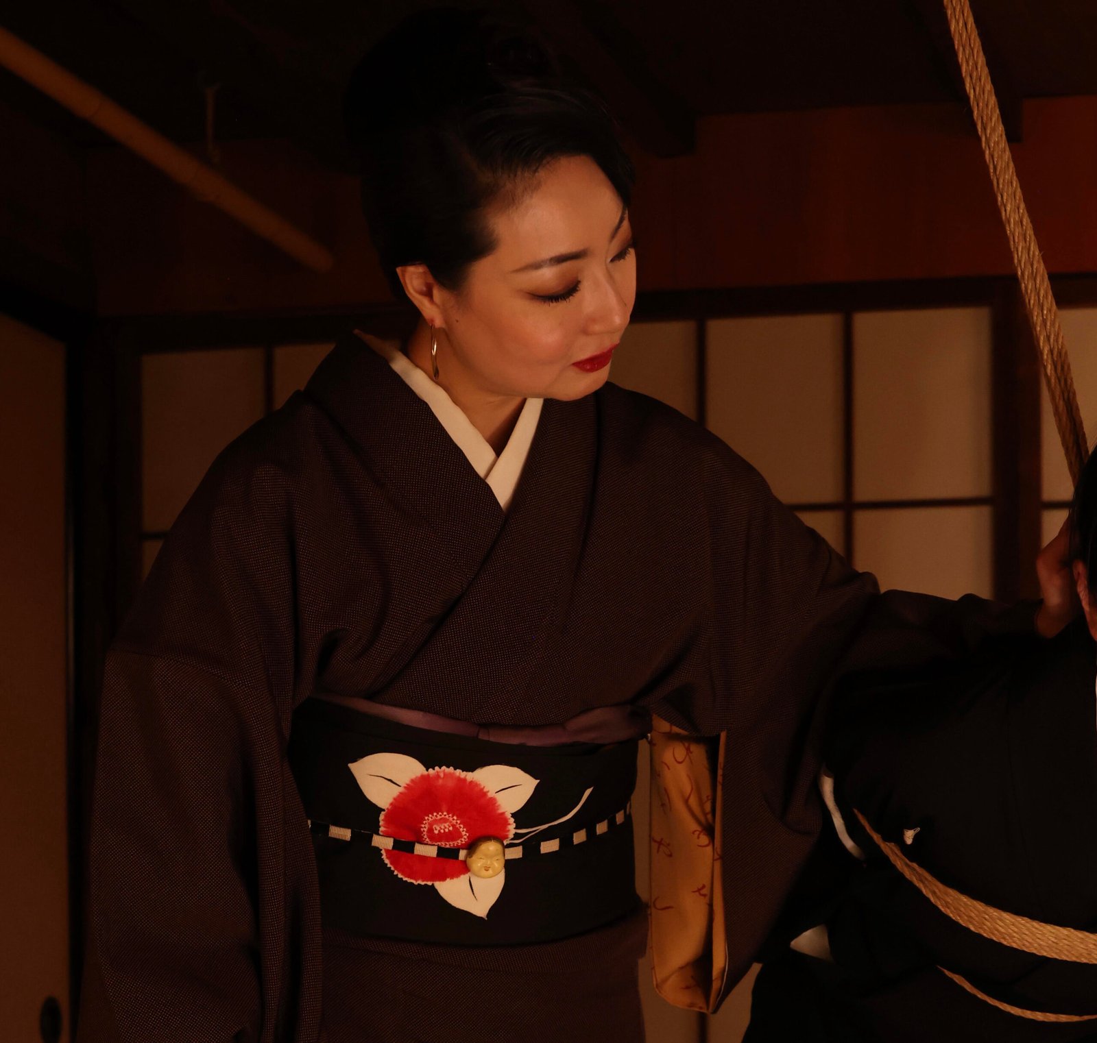 Woman in kimono beside bound person indoors